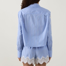 Model wearing Jonathan Simkhai Renata Cropped Embellished Shirt in Oxford Blue Stripe, rear view, with white lace-hem shorts