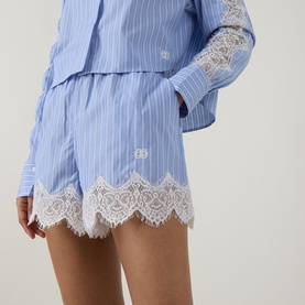 Model wearing Jonathan Simkhai Emmie Stripe Lace Shorts in Oxford Blue Stripe with white scalloped lace trim, styled with matching striped shirt.