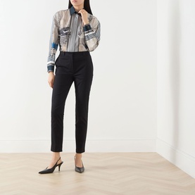 Model wearing Max Mara Studio black slim-leg cotton trousers, styled with a printed shirt and black slingback heels.