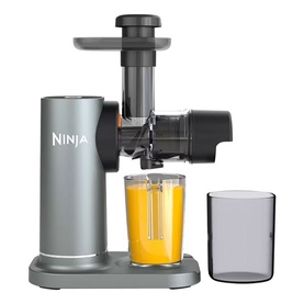 Ninja slow juicer in silver and black with a glass of fresh orange juice and a smoke-grey collection cup alongside