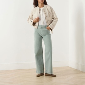 Model wearing Paige Wide Leg Jeans in Vintage Seaglass, styled with a beige bomber jacket, white top and taupe loafers.