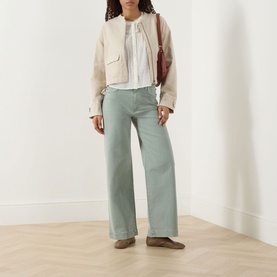 Model wearing Paige Wide Leg Jeans in Vintage Seaglass, styled with a cream jacket, white blouse, and brown loafers, carrying a burgundy bag.