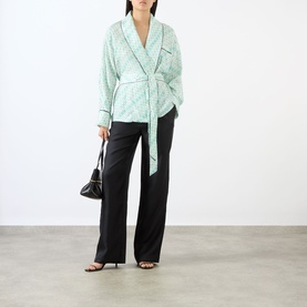 Model wearing Victoria Beckham Alba Silk Printed Wrap Blouse in blue with shawl collar and self-tie belt, styled with black wide-leg trousers