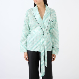 Model wearing Victoria Beckham Alba Silk Printed Wrap Blouse in blue with contrast piping, shawl collar and self-tie belt, styled with black trousers