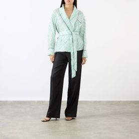 Model wearing Victoria Beckham Alba Silk Printed Wrap Blouse in blue with contrast piping and self-tie belt, styled with black wide-leg trousers.