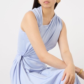 Model wearing Victoria Beckham Cloud Blue dress with draped neckline and twist-knot waist detail, styled with gold jewellery