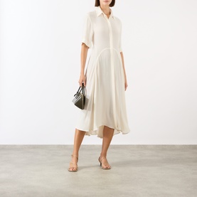 Model wearing Victoria Beckham Panelled Shirt Dress in white, midi length with flared skirt and high-low hem, styled with a grey bag and nude sandals.