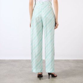 Model wearing Victoria Beckham blue wide-leg trousers with geometric print, shown from behind, styled with black heels.