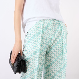Model wearing Victoria Beckham blue chain-print wide-leg trousers with white top, carrying a small black clutch bag.
