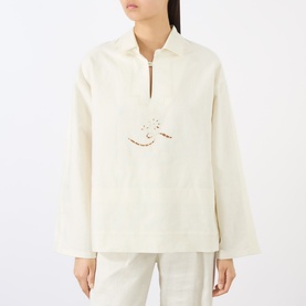 Model wearing Victoria Beckham white long-sleeve zip-neck top with embroidered chest detail, styled with matching white trousers.