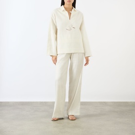 Model wearing Victoria Beckham white oversized top with ring detail, styled with matching wide-leg trousers and strappy heels.