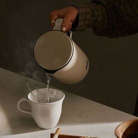 Aarke Kettle Sand in cream being poured into a white mug, styled with bread and jam on a wooden board