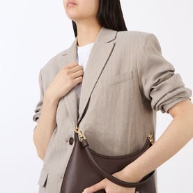 Model wearing Anine Bing linen blazer in neutral tone, styled with white tee. Model carries a dark brown shoulder bag with gold hardware.