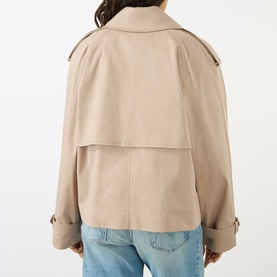 Model wearing Anine Bing beige cotton trench coat, rear view showing cape panel and cuffed sleeves, styled with light blue jeans.