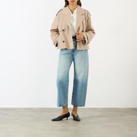 Model wearing Anine Bing beige cropped cotton trench coat, styled with white shirt, light wash wide-leg jeans and black kitten heel flats.