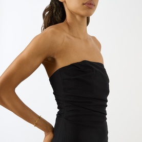 Model wearing Anine Bing black strapless ruched dress in viscose blend, styled with a gold chain bracelet.