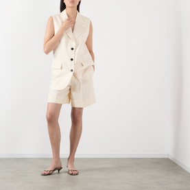 Model wearing Anine Bing cream gilet with matching shorts and strappy heeled sandals.