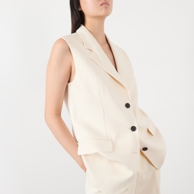 Model wearing Anine Bing cream gilet with black buttons, styled with matching cream shorts, hands in pockets.