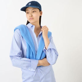 Model with Anine Bing Jeremy Logo Denim Baseball Cap in dark blue, worn with a light blue striped oversized shirt and blue knit draped over shoulder.