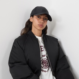 Model with Anine Bing Jeremy Logo Baseball Cap in black nylon with subtle sheen, styled with black bomber jacket and white graphic tee.