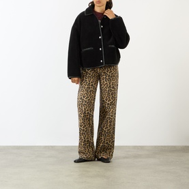 Model wearing Anine Bing black shearling jacket with contrast trim, styled with leopard print wide-leg trousers and black flats.