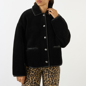 Model wearing Anine Bing black shearling jacket with leather trim, silver snap buttons, and patch pockets, styled with leopard-print trousers.