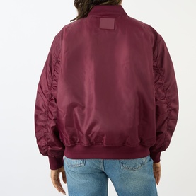 Model wearing Anine Bing Leon Bomber Jacket in burgundy, back view showing logo patch, subtle sheen, elasticated hem and stretch cuffs, styled with