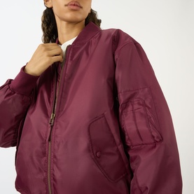 Model wearing Anine Bing Leon Bomber Jacket in burgundy, showing zip-through fastening, button flap pocket and subtle sheen finish.