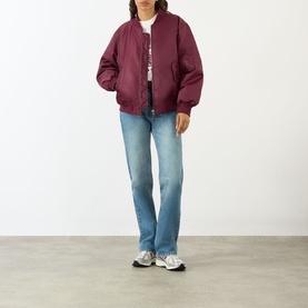 Model wearing Anine Bing Leon Bomber Jacket in burgundy with light-wash straight-leg jeans and grey trainers.