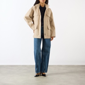 Model wearing Anine Bing Odin Utility Jacket in beige with four flap pockets, styled with blue wide-leg jeans and black heels.