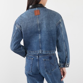 Model wearing Anine Bing washed blue denim jacket, back view, with black leather collar detail and brown logo patch, paired with matching denim jeans.