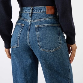 Model wearing Anine Bing Brie Twisted Seam Jeans in Cabana Blue, showing rear logo patch, twisted seams, and wide-leg fit. Styled with navy jumper.