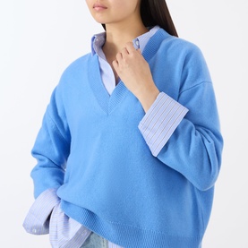 Model wearing Anine Bing blue cashmere V-neck sweater, styled over a blue striped shirt with visible collar and cuffs.