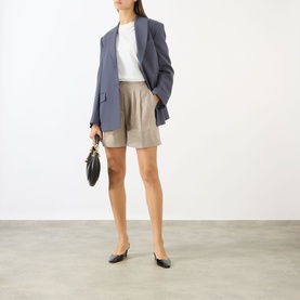 Model wearing Anine Bing shorts in taupe, styled with a blue oversized blazer, white top and black heels, carrying a black handbag.