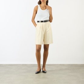 Model wearing Anine Bing cream tailored shorts with white tank top and black belt, styled with black flat shoes.