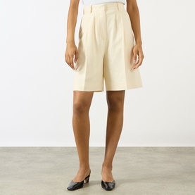 Model wearing Anine Bing cream tailored shorts with front pleats, styled with black kitten heel mules.