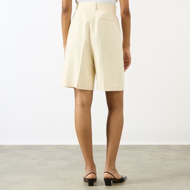 Model wearing Anine Bing cream tailored shorts, back view, styled with black strappy flat mules.