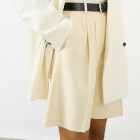 Model wearing Anine Bing cream pleated shorts with a black belt, styled with a cream oversized blazer.