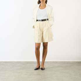 Model wearing Anine Bing cream pleated shorts with matching blazer, white vest, black belt and black ballet flats.