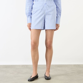 Model wearing Anine Bing Ramy Striped Shorts in washed blue with elasticated waistband, styled with a blue shirt and black ballet flats.