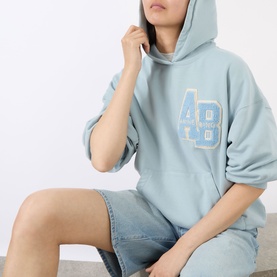 Model wearing Anine Bing Harvey Logo Drawstring Hoodie in blue with AB varsity chest logo, styled with denim shorts.