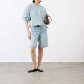 Model wearing Anine Bing Harvey Logo Drawstring Hoodie in blue, styled with light wash denim shorts and black flats, carrying a brown bag.