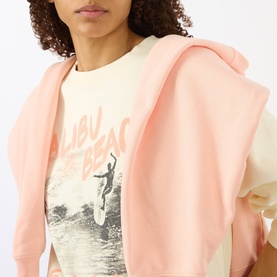 Model wearing Anine Bing Washed Buttercream Sweat Top with pink zip-up hoodie and Malibu Beach graphic tee
