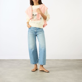 Model wearing Anine Bing Washed Buttercream Sweat Top with pink ruffled overlay, styled with light blue wide-leg jeans and tan flat sandals