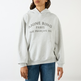 Model wearing Anine Bing grey cotton hoodie with Paris logo print, styled with blue denim jeans.