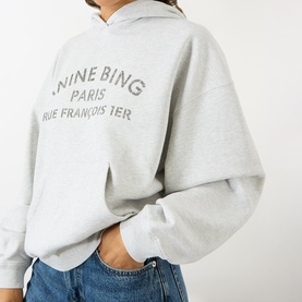 Model wearing Anine Bing grey cotton hoodie with Paris logo print, styled with blue denim jeans.