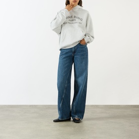 Model wearing Anine Bing grey cotton sweat top with logo print, styled with wide-leg blue jeans and black flat shoes.
