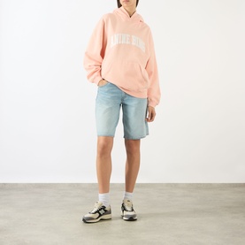 Model wearing Anine Bing blush oversized logo hoodie, styled with light-wash denim shorts, white socks and grey trainers.