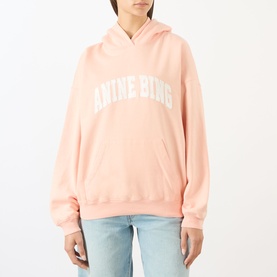 Model wearing Anine Bing blush hoodie sweat top with bold logo print, styled with light blue jeans.