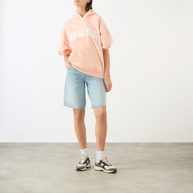 Model wearing Anine Bing blush short-sleeve logo hoodie, styled with light wash denim shorts and multicolour trainers.